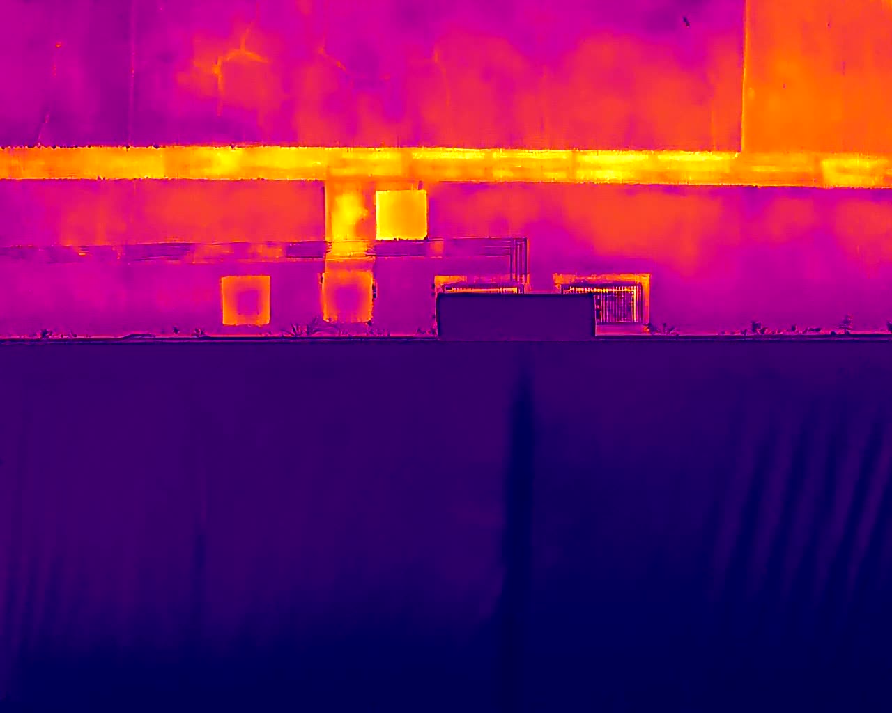 Image thermique d'un bâtiment : la chaleur s'échappe en jaune vif par les ouvertures, les surfaces isolées restent violettes